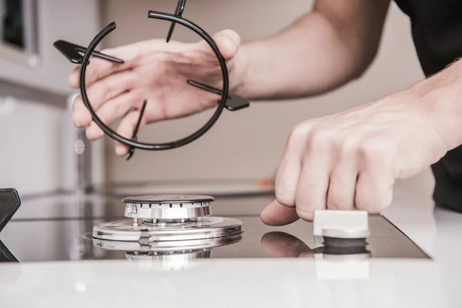 Hands lifting a grate and burner cap off a gas cooktop